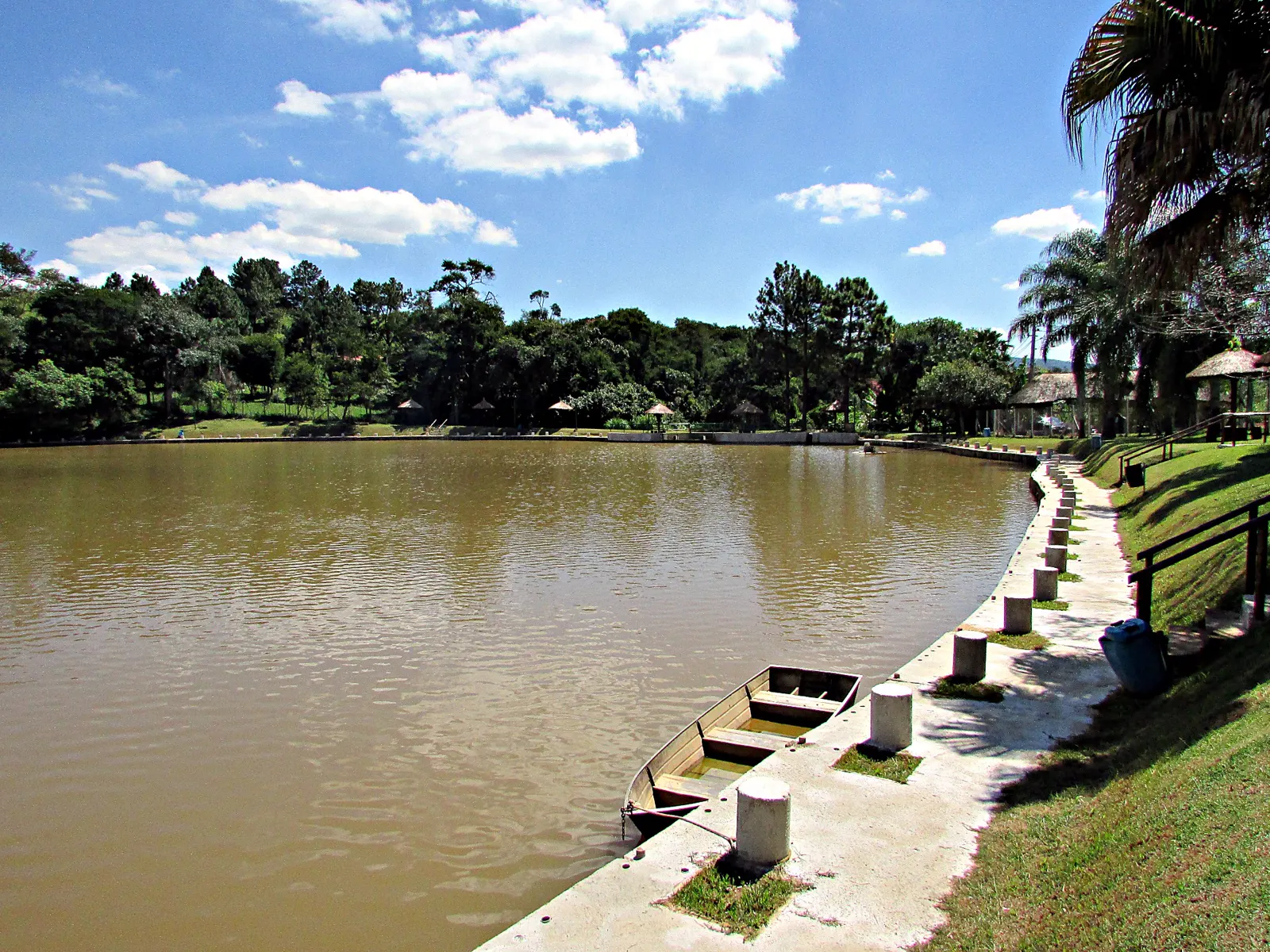 Lago do pesqueiro com céu azul, mata ao fundo e pesqueiros na margem