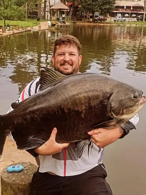 Pescador sorridente com tambaqui, restaurante ao fundo