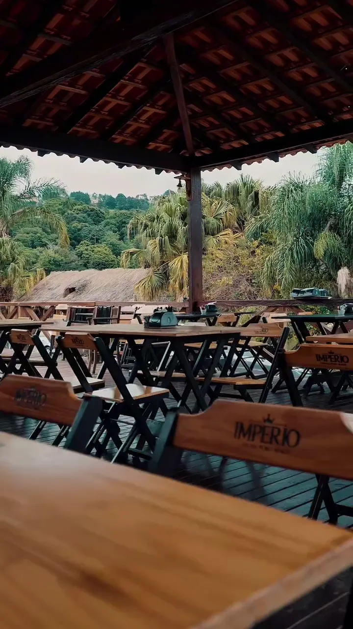Deck de madeira com mesas e guarda-sóis, cercado de verde